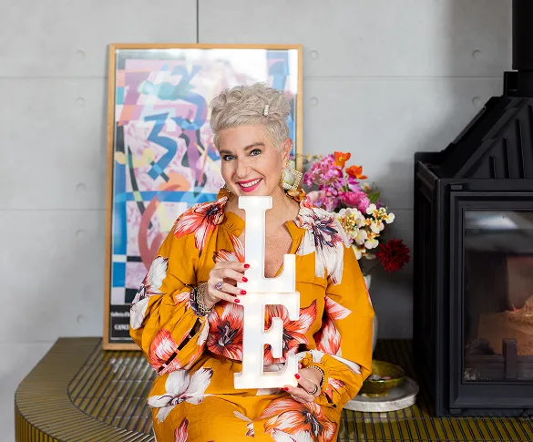 Dr Leanne Elich in a floral dress holding "LE" letters for her sales consulting service indoors